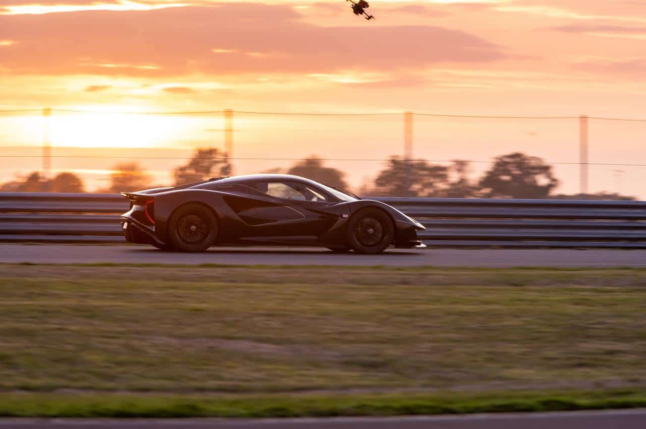 Dunkler Lotus Evija in Seitenansicht auf einer Rennstrecke bei Sonnenuntergang, über ihm fliegt eine Kameradrohne